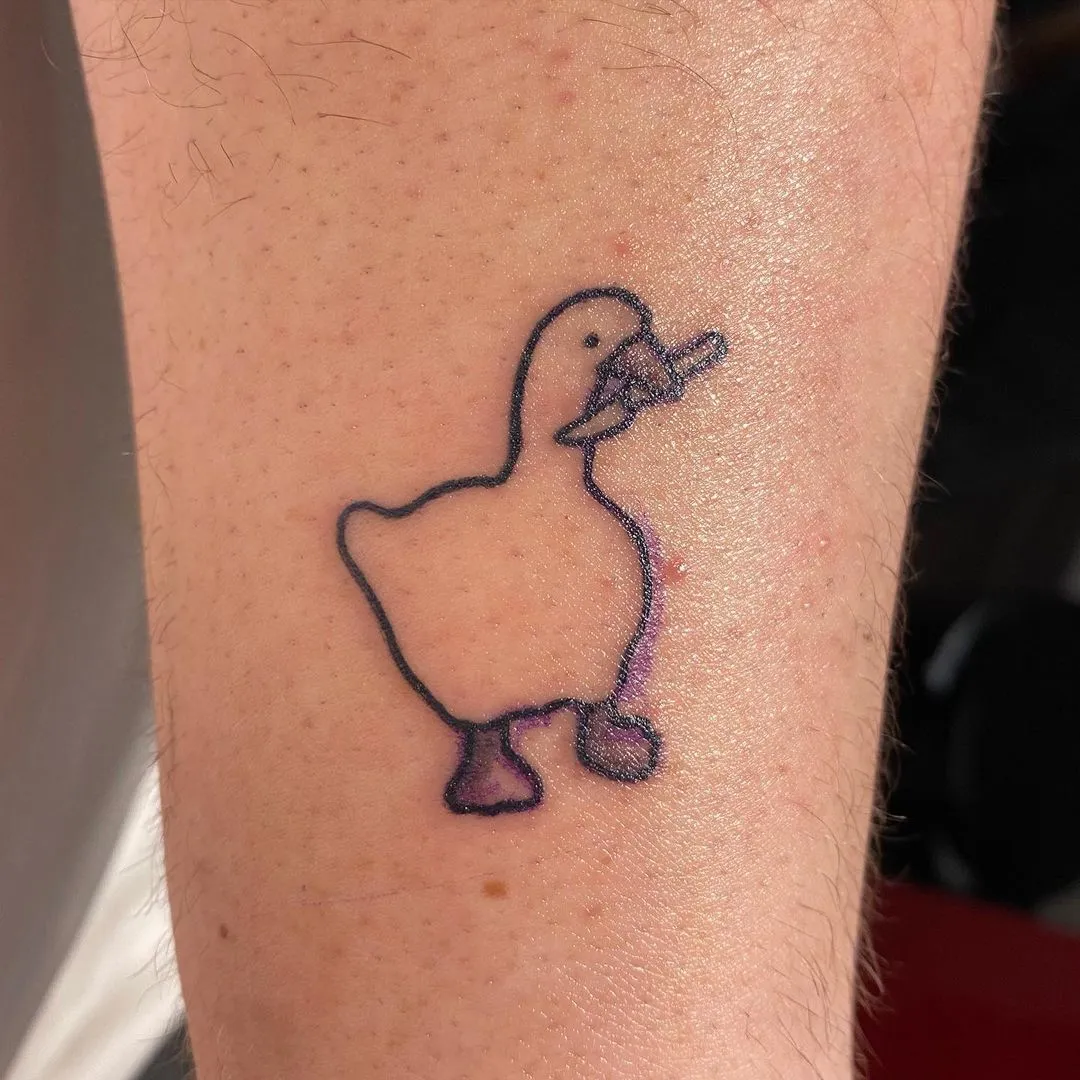 A picture of an arm with a tatoo of a goose. The goose is holding a small knife in its beak